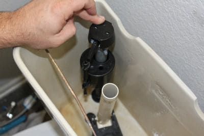Man's hand touching toilet fill valve
